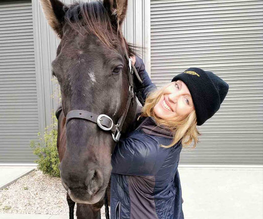 Annette Kaitinis wearing yellow Scoot Boot tights hugging her black horse in her driveway