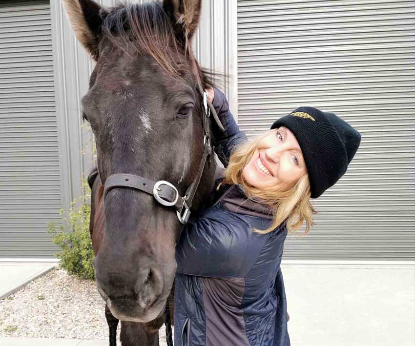 Annette Kaitinis wearing yellow Scoot Boot tights hugging her black horse in her driveway